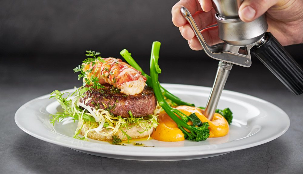 Foodstylist spritzt Espuma auf Teller